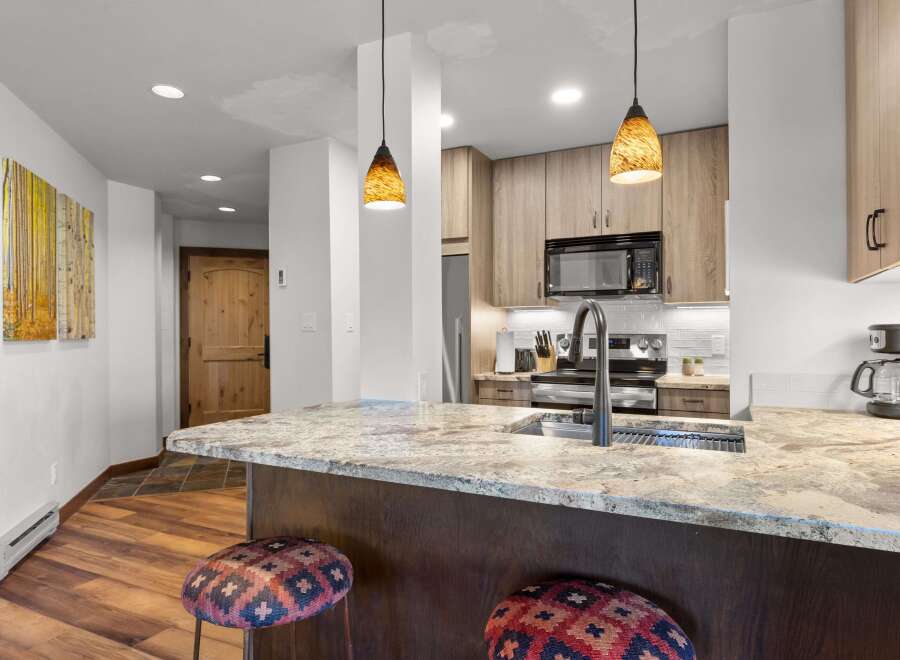 This modern kitchen boasts a spacious granite island with a deep sink and a sleek faucet, perfect for meal preparation and casual dining.