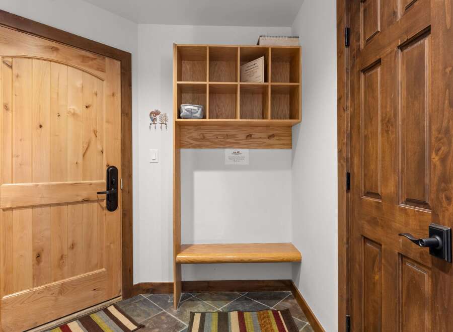 Welcome guests into this charming entryway featuring a light wood door with a black handle, complemented by a rustic wooden shelf and bench unit.