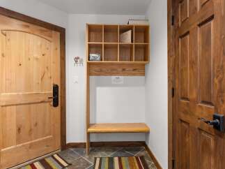Welcome guests into this charming entryway featuring a light wood door with a black handle, complemented by a rustic wooden shelf and bench unit.