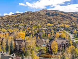 Experience the beauty of autumn in this stunning mountain community, featuring a cluster of residential buildings nestled amongst vibrant fall foliage.