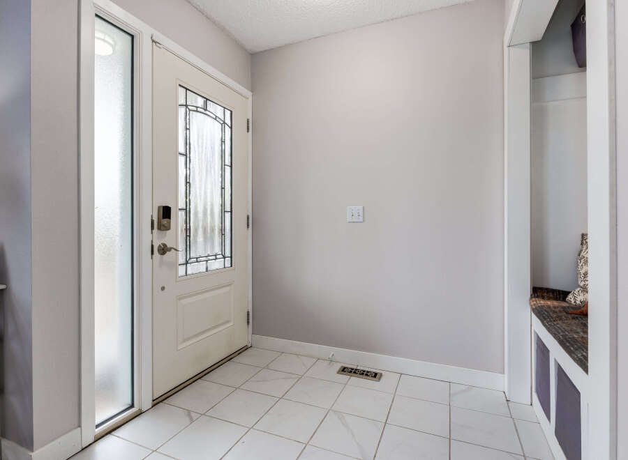 Step into a welcoming entryway featuring a stylish white door with frosted glass and decorative panels, complemented by sleek tile flooring.