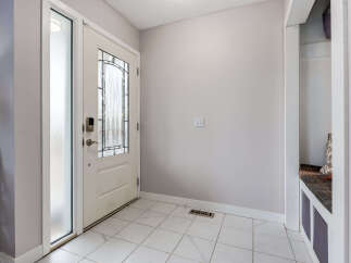 Step into a welcoming entryway featuring a stylish white door with frosted glass and decorative panels, complemented by sleek tile flooring.