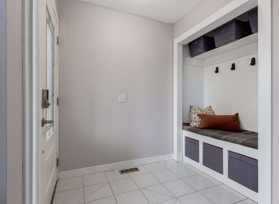 This entryway features a white door with a glass panel and a modern lock, leading into a space with light gray walls and tiled flooring.