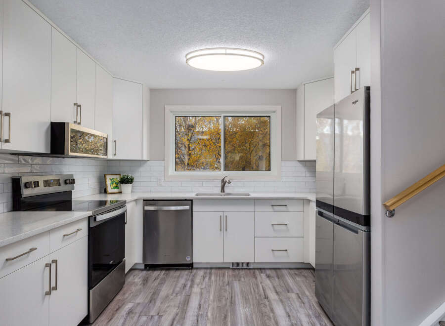 This modern kitchen boasts sleek white cabinetry and stainless steel appliances, including a refrigerator, dishwasher, and oven.