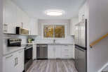 This modern kitchen boasts sleek white cabinetry and stainless steel appliances, including a refrigerator, dishwasher, and oven.