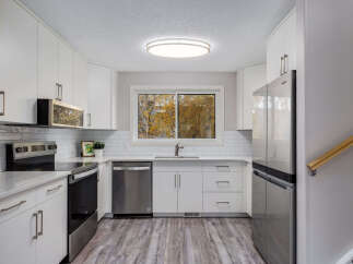 This modern kitchen boasts sleek white cabinetry and stainless steel appliances, including a refrigerator, dishwasher, and oven.