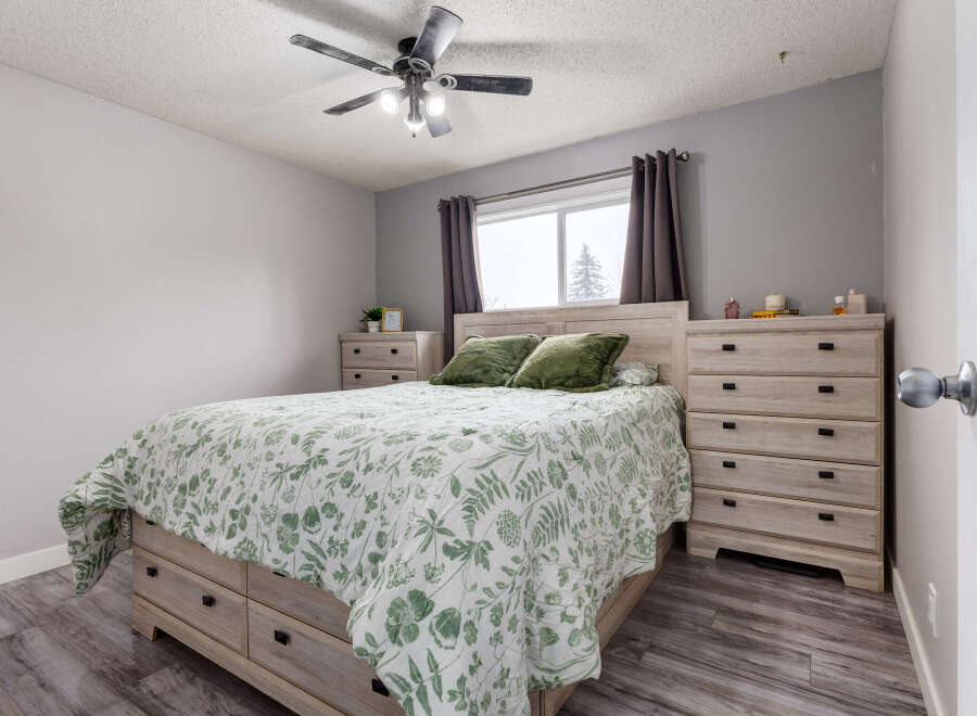 This bedroom features a light wood bed frame with built-in drawers, complemented by matching nightstands and dressers.