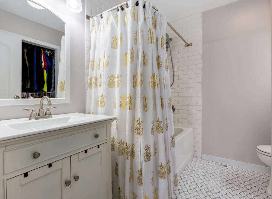 This charming bathroom features a white vanity with a brushed nickel faucet and a large mirror reflecting a closet with organized clothing.