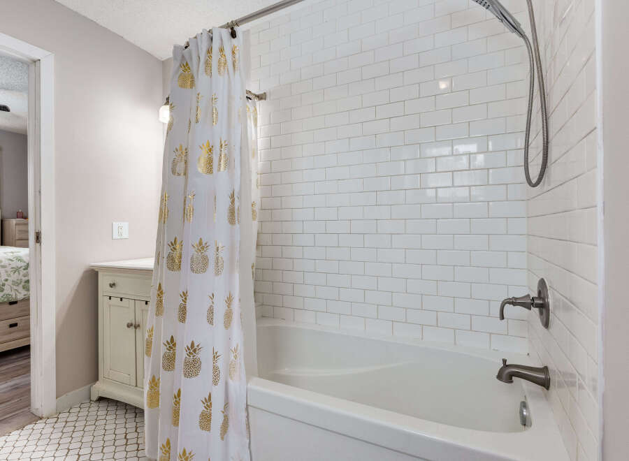 Step into this charming bathroom featuring a classic white subway tile shower and tub surround, complemented by a stylish white shower curtain adorned with a gold pineapple pattern.