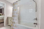 Step into this charming bathroom featuring a classic white subway tile shower and tub surround, complemented by a stylish white shower curtain adorned with a gold pineapple pattern.