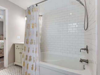Step into this charming bathroom featuring a classic white subway tile shower and tub surround, complemented by a stylish white shower curtain adorned with a gold pineapple pattern.