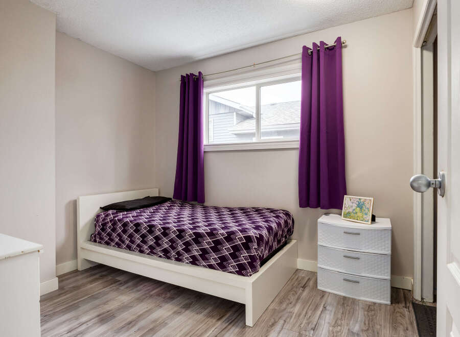This cozy bedroom features a comfortable white bed adorned with a striking purple geometric-patterned comforter and a black pillow.
