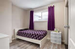 This cozy bedroom features a comfortable white bed adorned with a striking purple geometric-patterned comforter and a black pillow.