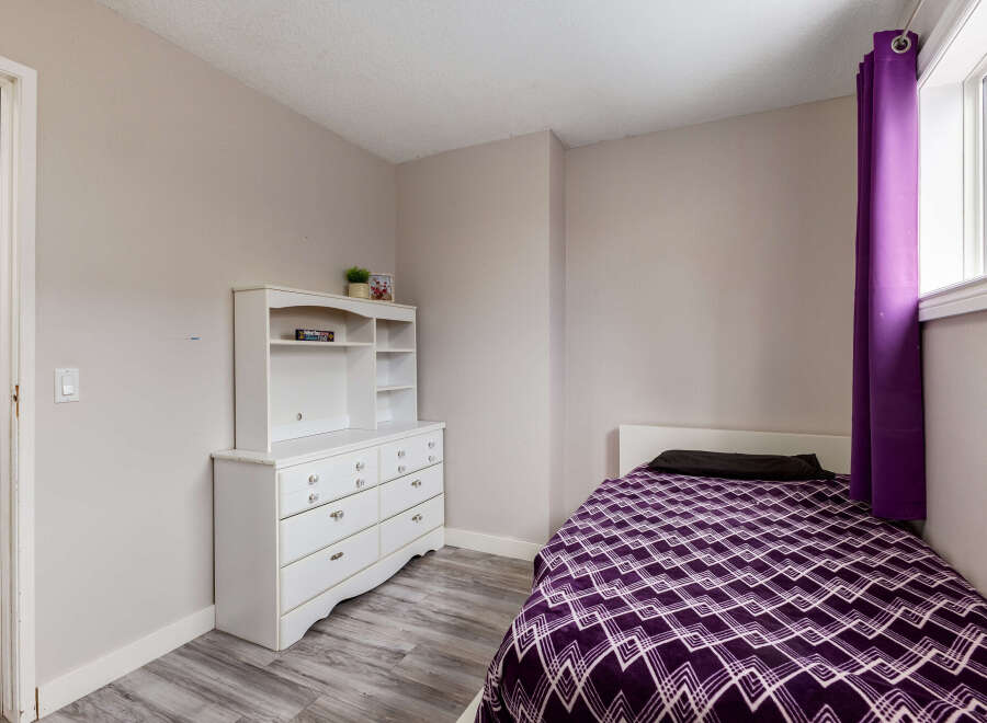 This cozy bedroom features a comfortable single bed adorned with a vibrant purple geometric-patterned comforter and a dark pillow.