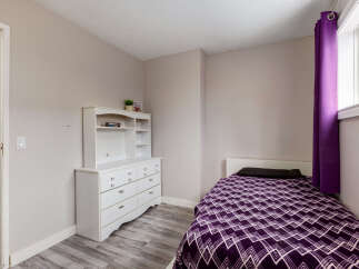 This cozy bedroom features a comfortable single bed adorned with a vibrant purple geometric-patterned comforter and a dark pillow.