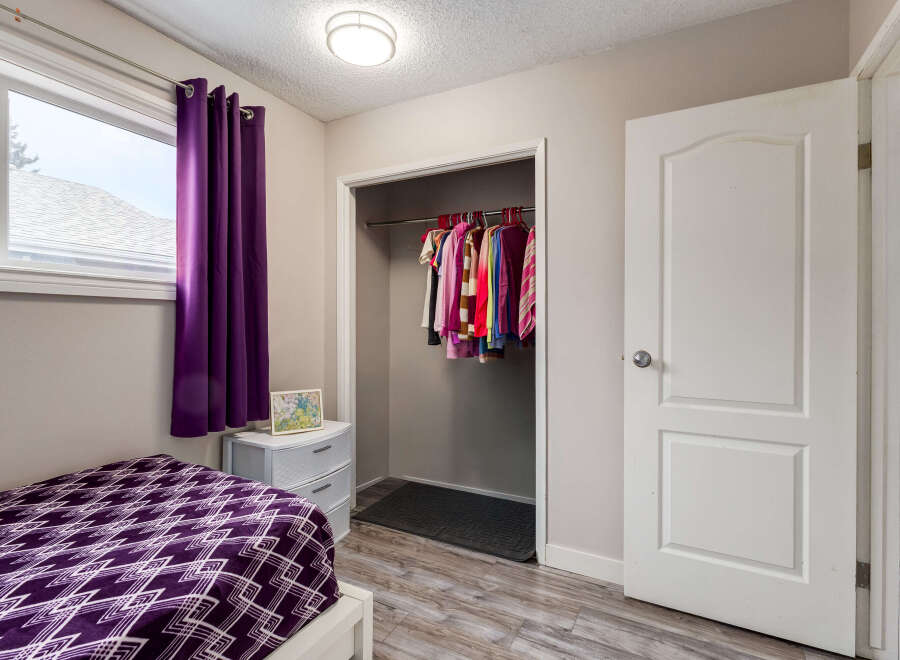 This bedroom features a cozy bed with a vibrant purple geometric-patterned comforter, complemented by matching purple curtains.