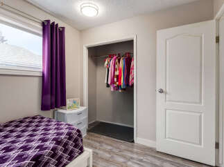 This bedroom features a cozy bed with a vibrant purple geometric-patterned comforter, complemented by matching purple curtains.