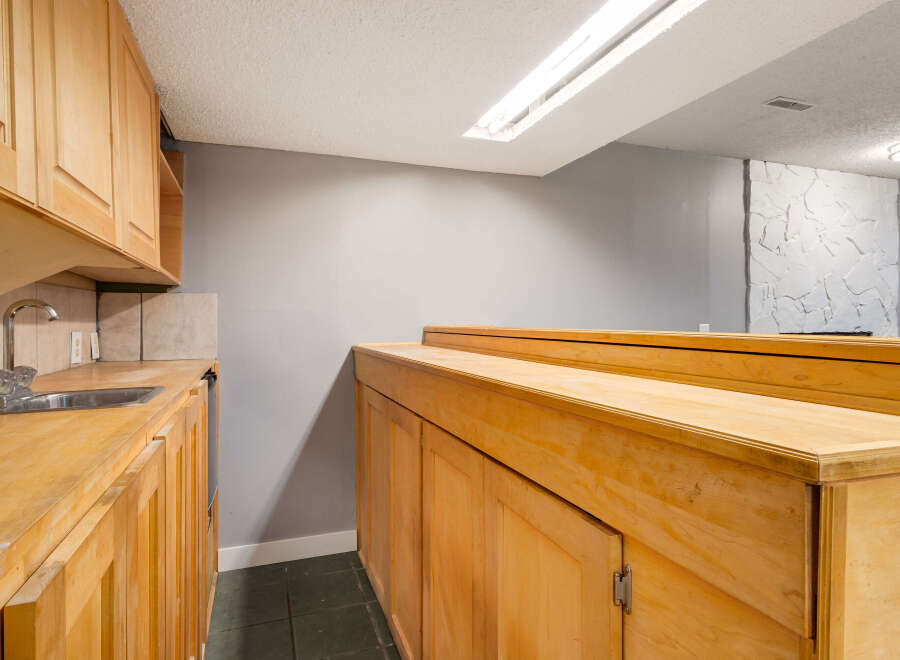This basement area features a functional wet bar with light wood cabinetry and a stainless steel sink, perfect for entertaining.