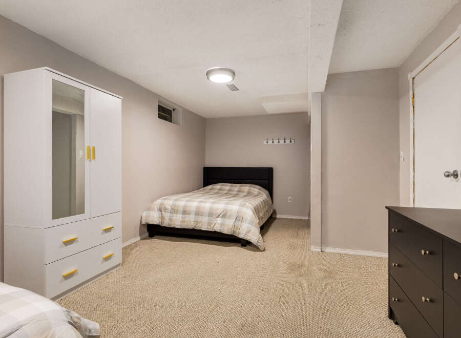 This basement bedroom offers a comfortable and functional space with a queen-size bed featuring a neutral plaid comforter.