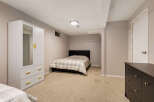 This basement bedroom offers a comfortable and functional space with a queen-size bed featuring a neutral plaid comforter.