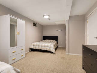 This basement bedroom offers a comfortable and functional space with a queen-size bed featuring a neutral plaid comforter.