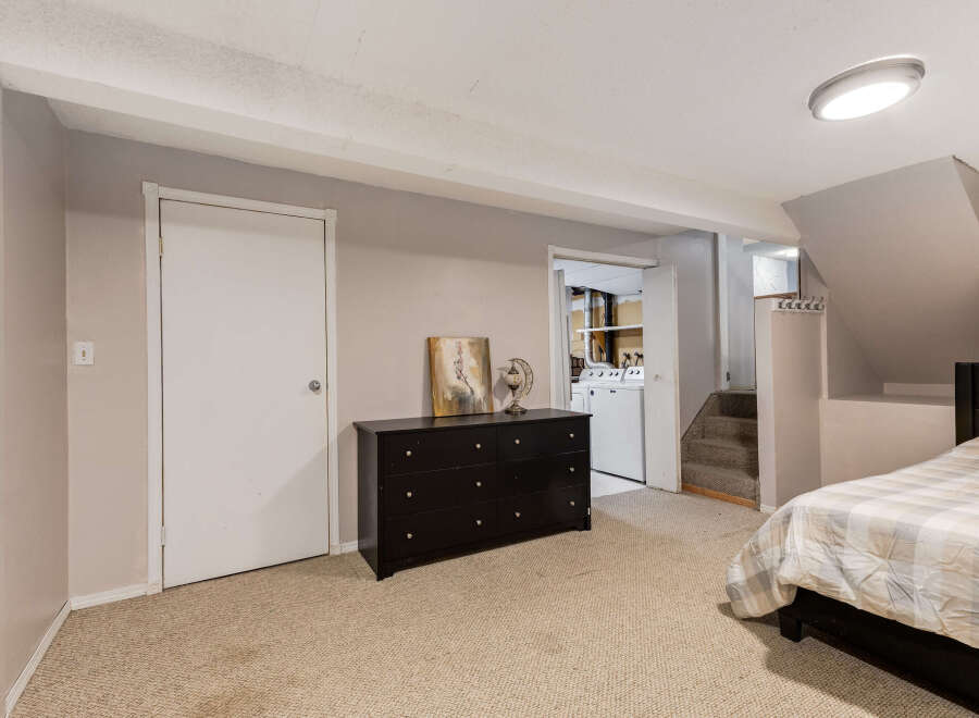 Discover comfortable living in this basement bedroom, featuring a plush carpeted floor and a convenient dresser for storage.