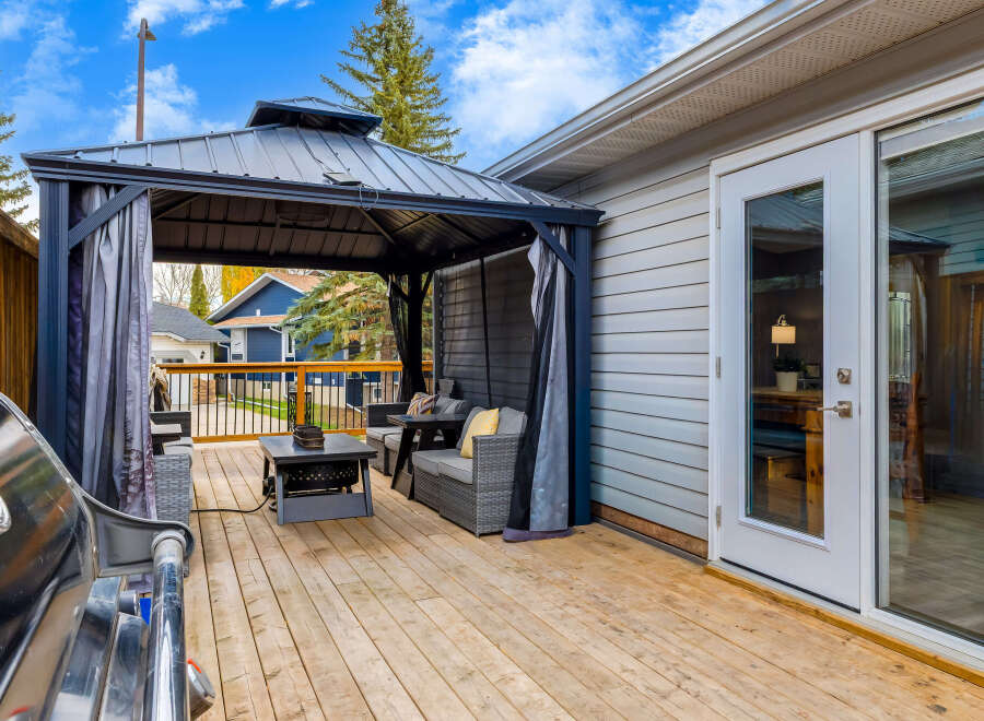Step onto a spacious wooden deck, perfect for outdoor entertaining, featuring a covered gazebo with comfortable seating and a stylish coffee table.