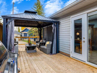Step onto a spacious wooden deck, perfect for outdoor entertaining, featuring a covered gazebo with comfortable seating and a stylish coffee table.