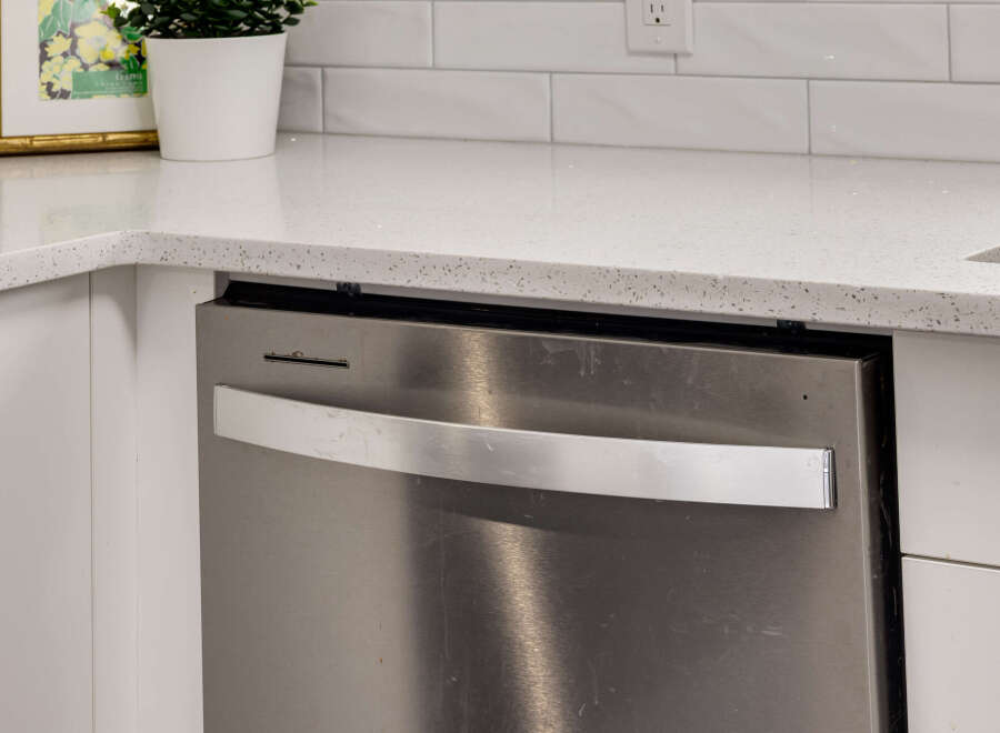 Discover a modern kitchen featuring a sleek stainless steel dishwasher integrated seamlessly with white cabinetry.