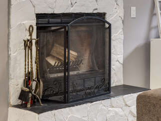 Cozy up by this inviting fireplace, featuring a rustic stone surround and a protective black mesh screen.