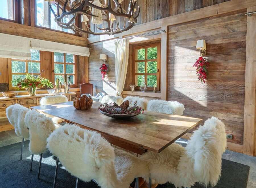 Experience rustic elegance in this charming dining room, featuring a large wooden table surrounded by plush, sheepskin-covered chairs.