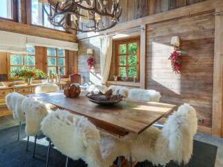 Experience rustic elegance in this charming dining room, featuring a large wooden table surrounded by plush, sheepskin-covered chairs.