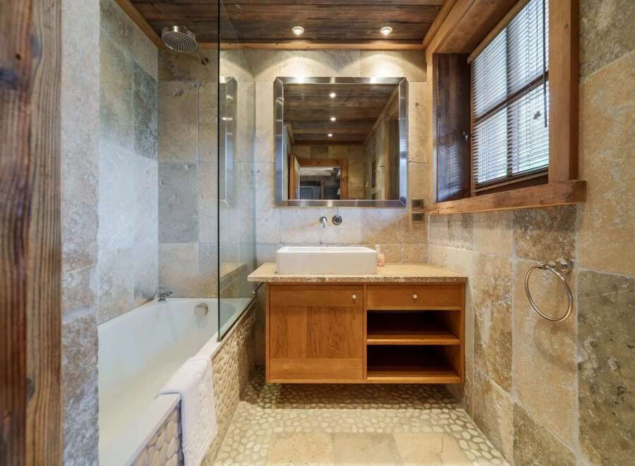 Experience rustic charm in this beautifully appointed bathroom, featuring a luxurious bathtub and a modern vessel sink atop a wooden vanity.