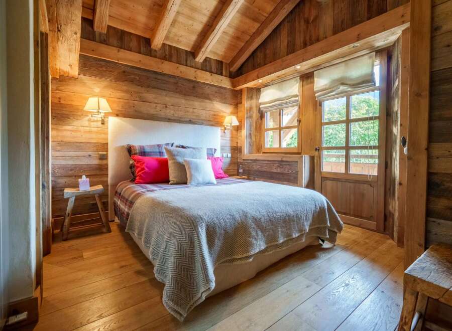 Experience rustic charm in this beautifully appointed bedroom, featuring warm wooden walls and a vaulted ceiling with exposed beams.