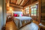 Experience rustic charm in this beautifully appointed bedroom, featuring warm wooden walls and a vaulted ceiling with exposed beams.