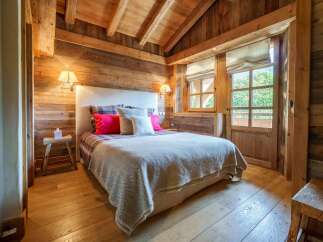 Experience rustic charm in this beautifully appointed bedroom, featuring warm wooden walls and a vaulted ceiling with exposed beams.