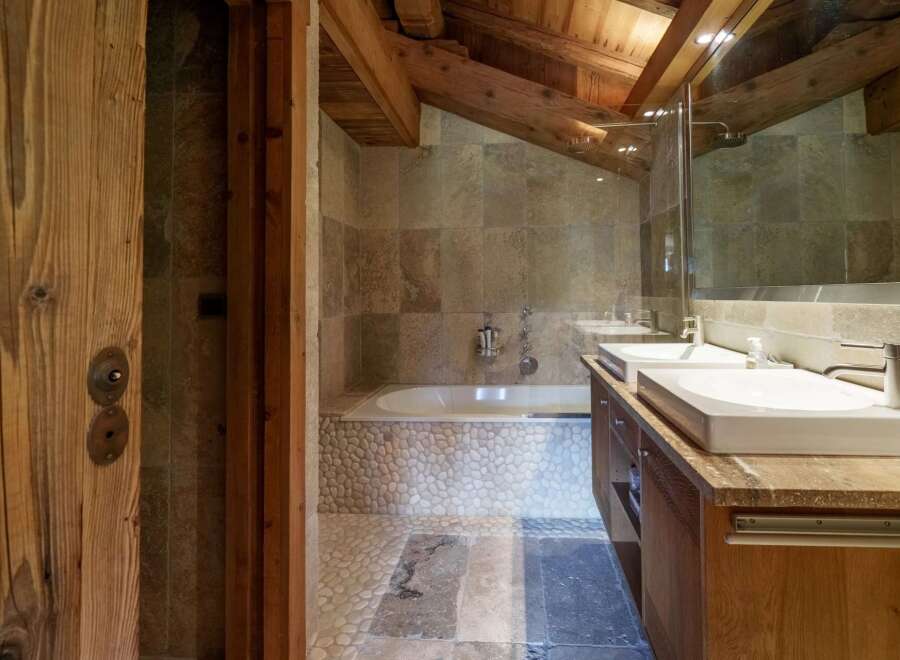 Experience rustic luxury in this charming bathroom, featuring a deep soaking tub surrounded by natural stone and pebble accents.
