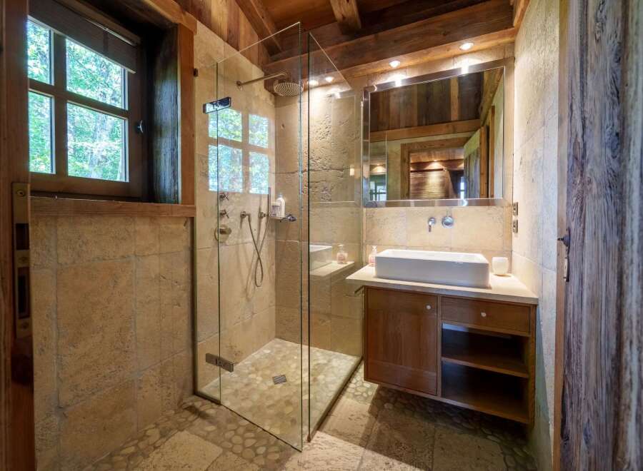 Experience rustic luxury in this charming bathroom, featuring a spacious walk-in shower with a rainfall showerhead and elegant stone tilework.