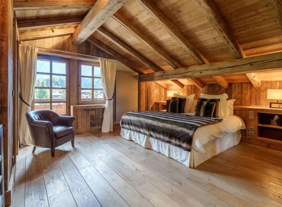 Experience rustic luxury in this charming attic bedroom, featuring exposed wooden beams and a cozy, inviting atmosphere.