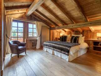 Experience rustic luxury in this charming attic bedroom, featuring exposed wooden beams and a cozy, inviting atmosphere.
