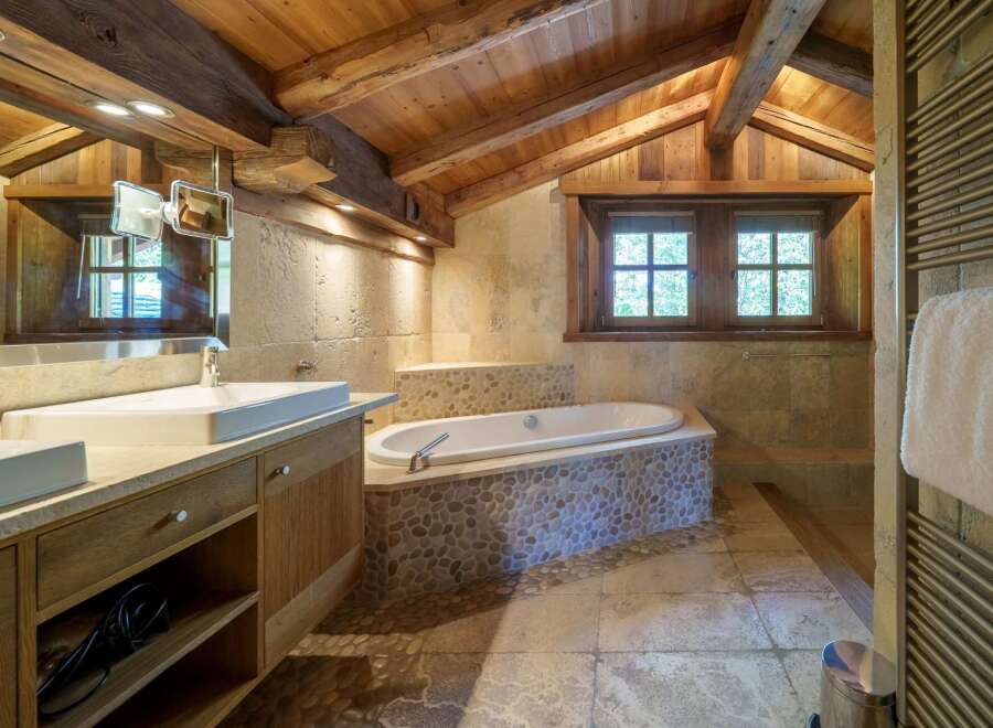 Experience rustic luxury in this charming bathroom, featuring a deep soaking tub nestled against a stone accent wall.
