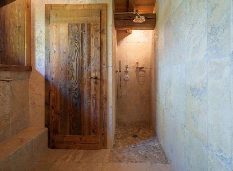 Experience rustic charm in this bathroom featuring a unique wooden door and a spacious walk-in shower.