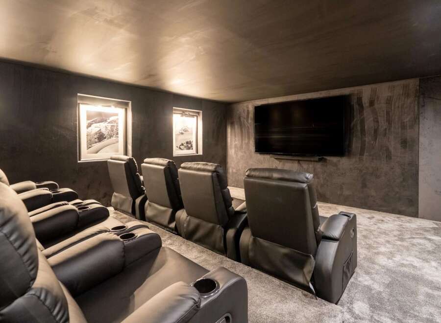 Experience cinematic luxury in this modern home theater, featuring plush black leather recliners with built-in cup holders for ultimate comfort.
