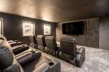 Experience cinematic luxury in this modern home theater, featuring plush black leather recliners with built-in cup holders for ultimate comfort.