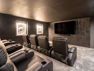 Experience cinematic luxury in this modern home theater, featuring plush black leather recliners with built-in cup holders for ultimate comfort.