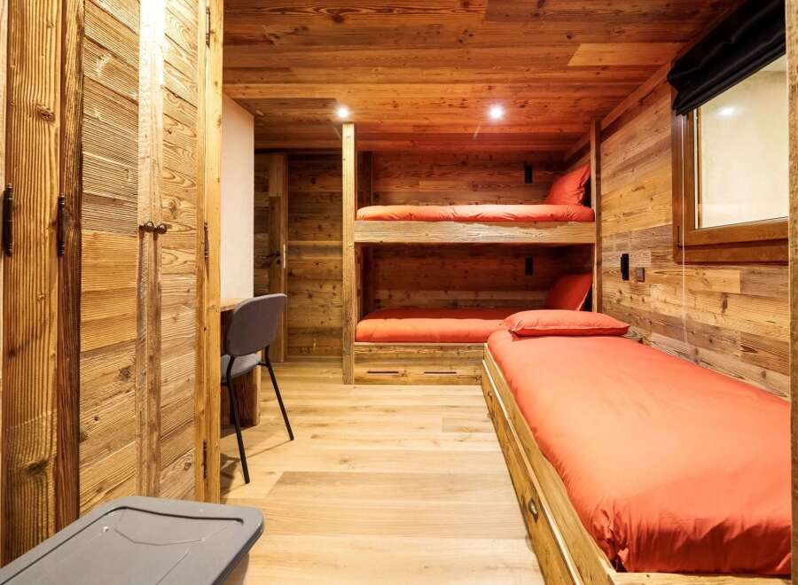 Experience cozy living in this charming wooden cabin bedroom, featuring a space-saving bunk bed and a comfortable single bed, both adorned with vibrant orange linens.