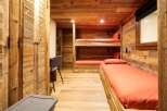 Experience cozy living in this charming wooden cabin bedroom, featuring a space-saving bunk bed and a comfortable single bed, both adorned with vibrant orange linens.