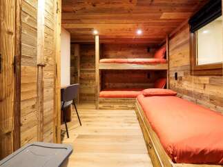 Experience cozy living in this charming wooden cabin bedroom, featuring a space-saving bunk bed and a comfortable single bed, both adorned with vibrant orange linens.