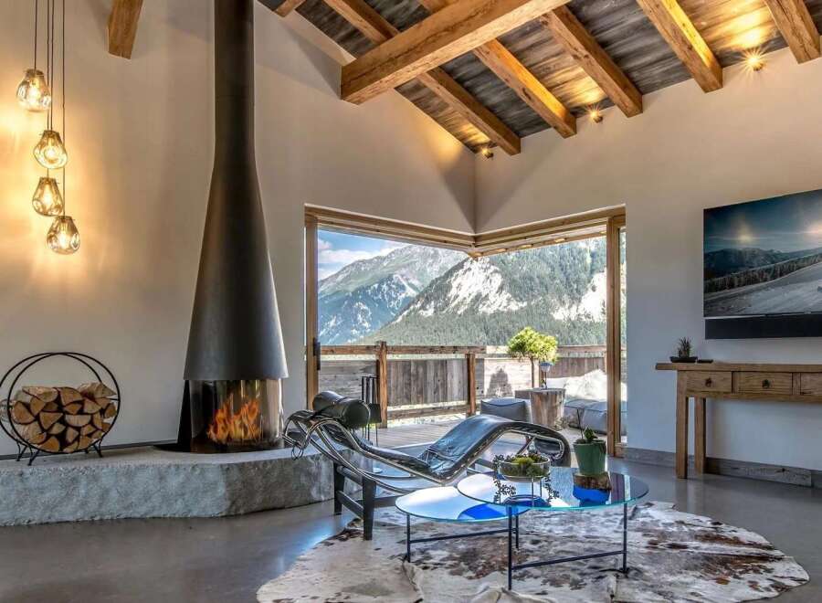 Experience breathtaking mountain views from this luxurious living room, featuring a modern fireplace and a sleek chaise lounge.