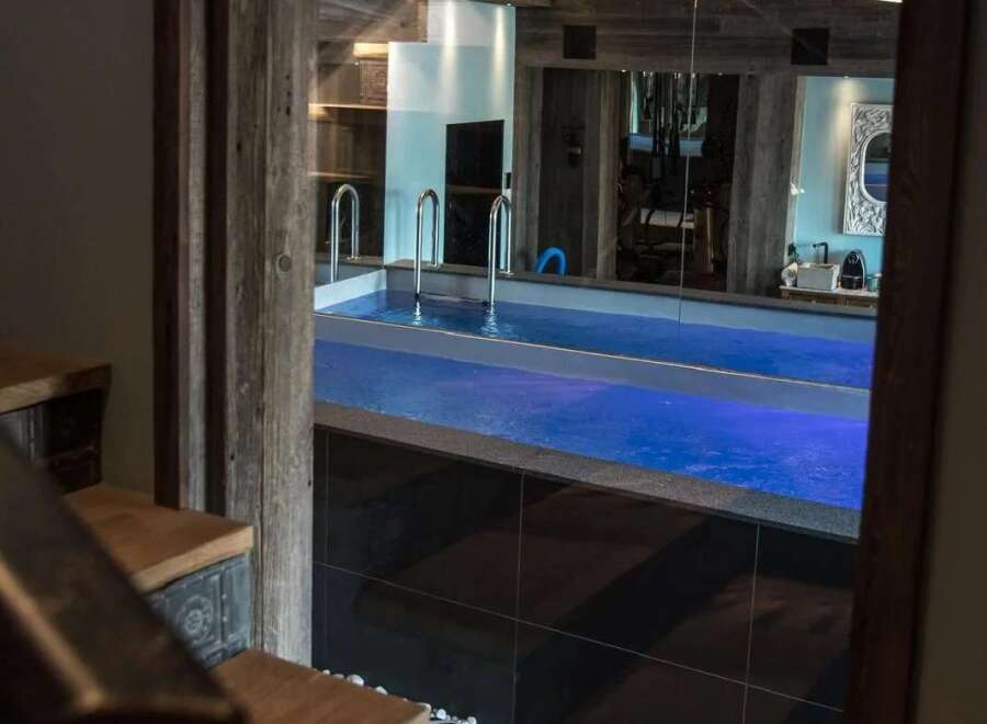 Step down into a luxurious indoor swimming pool area, complete with vibrant blue lighting and sleek chrome railings.